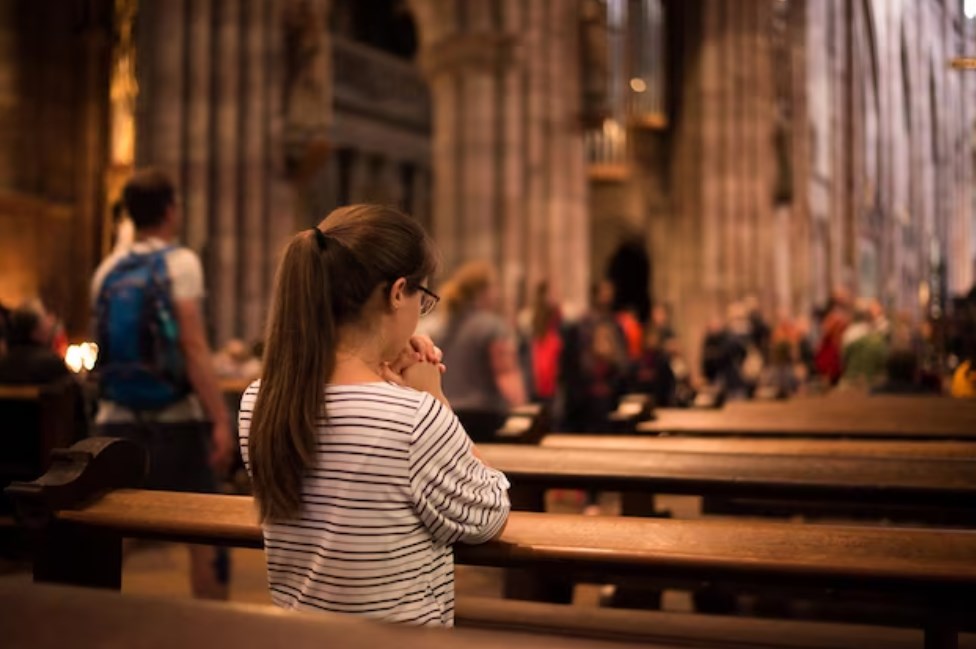 a young religious woman in glasses with long dark hair praying in a catholic cathedral