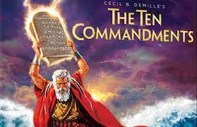 Movie cover of The Ten Commandments (1956) with purple background and an elderly man dressed in traditional attire holding a tablet inscribed with ancient writings.