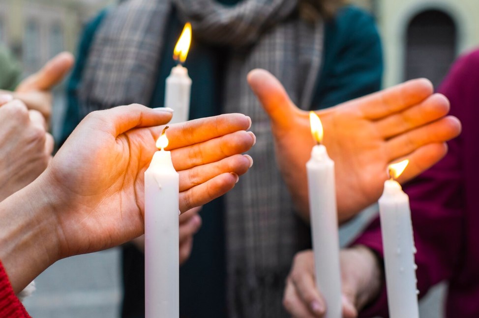 a side view of people’s hands holding candles