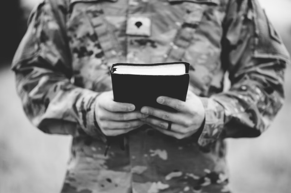 a grayscale shot of a young soldier holding a bible
