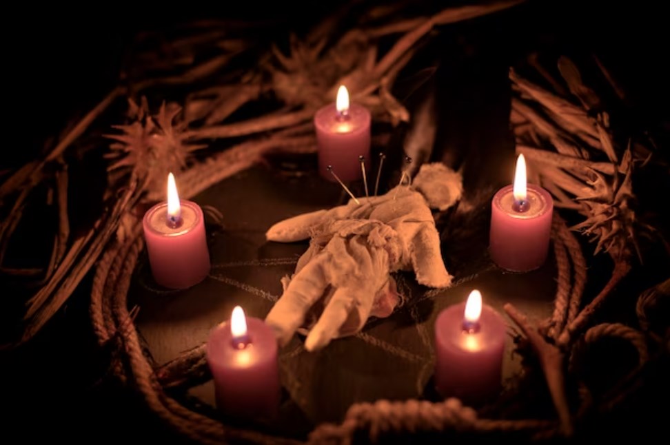 a voodoo rag doll with sticking needles surrounded by burning red candles