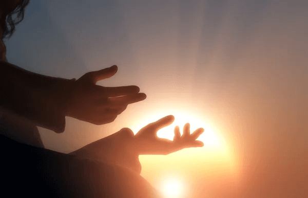 2 hands of a person praying in sunset