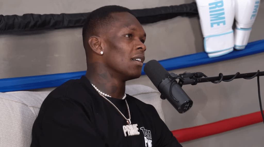 Israel Adesanya in black t-shirt sitting on the couch speaking to the microphone