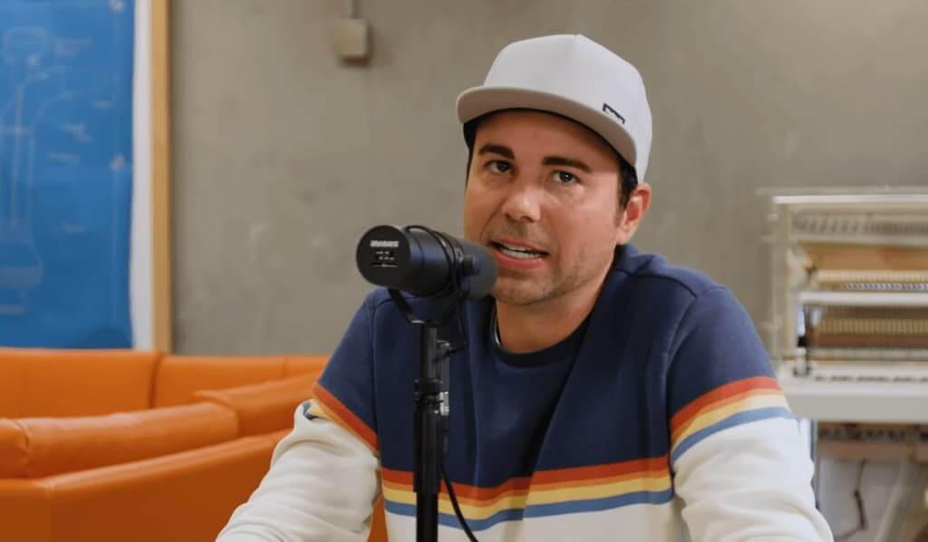 Mark Rober in a colorful sweater sitting near the microphone