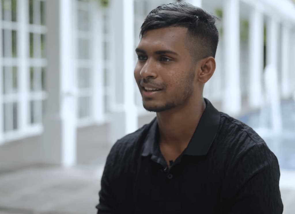 Matheesha Pathirana in black shirt sitting from the side near the white building outside