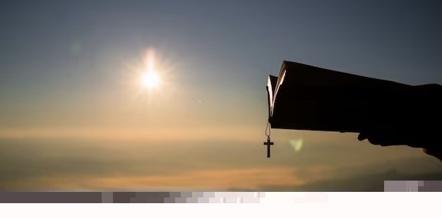 Silhouette of a human hand holding a Bible and a cross