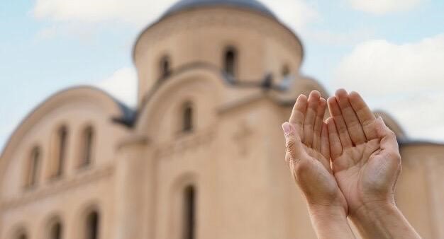 Hands clasped together against the background of a church