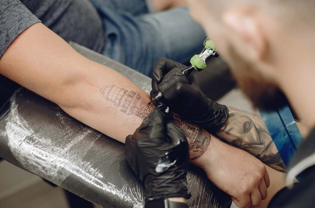A tattoo artist works on a detailed arm tattoo in a studio setting