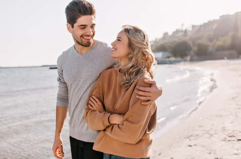 A happy couple embracing on a beach, smiling and enjoying the moment