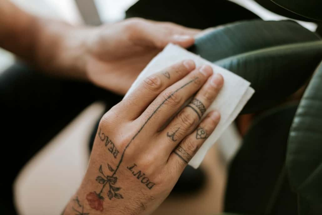 A tattooed hand wipes with a napkin, showing word and flower tattoos
