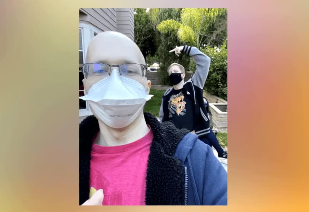 men in masks making the selfie, one in glasses and pink t-shirt, the second in black mask