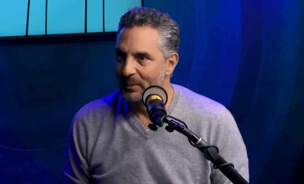 Mauricio Umansky in a gray sweater sitting near the microphone in blue color room