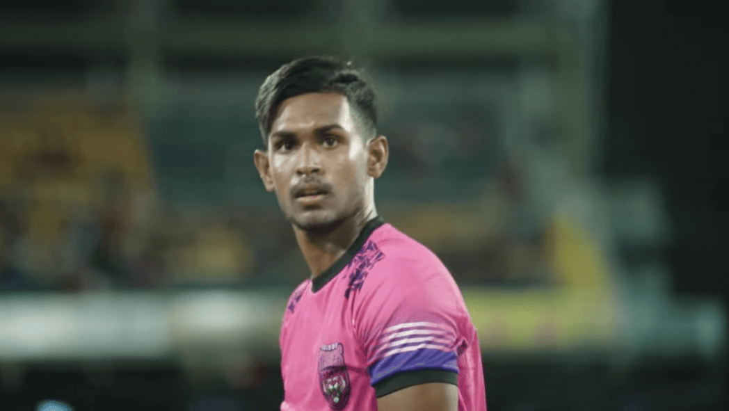 Matheesha Pathirana in a pink t-shirt on the field, the audience on the blurred background behind him
