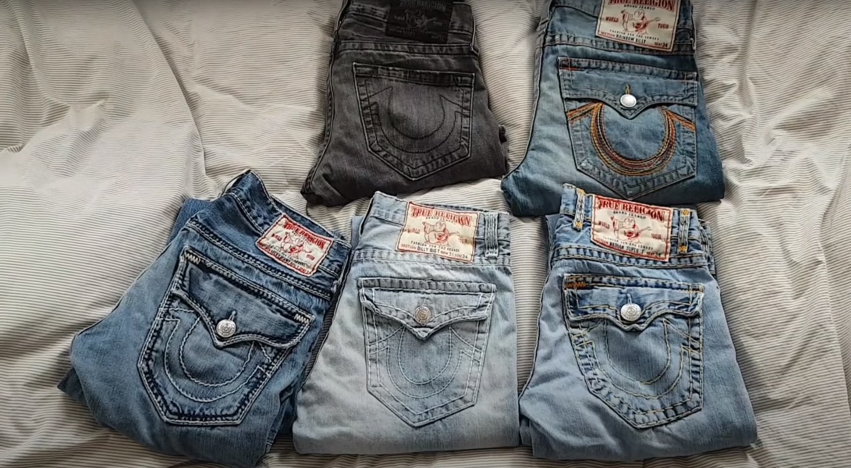 five pairs of different True Religion jeans laying folded on a white background
